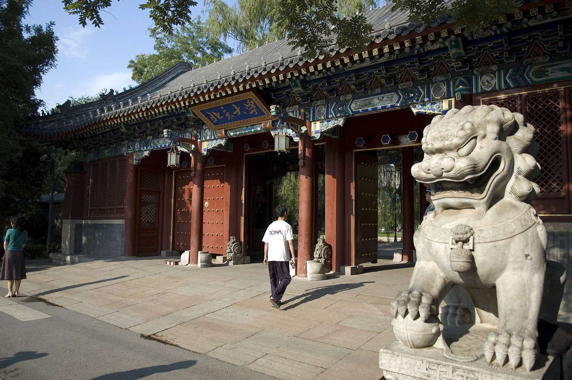 A side view of the traditional red gate at Peking University with a stone lion statue.